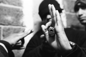 Black and white photo of two individuals, one holding a gun with hand around gun barrel