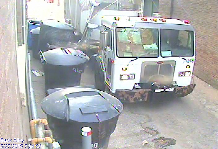 A truck down an alley emptying trash cans.